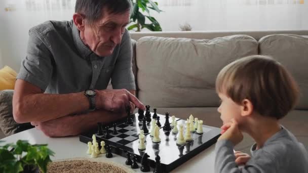 Anciano abuelo mayor aprendiendo un niño de 4 años jugando ajedrez, sentado en una mesa — Vídeo de stock