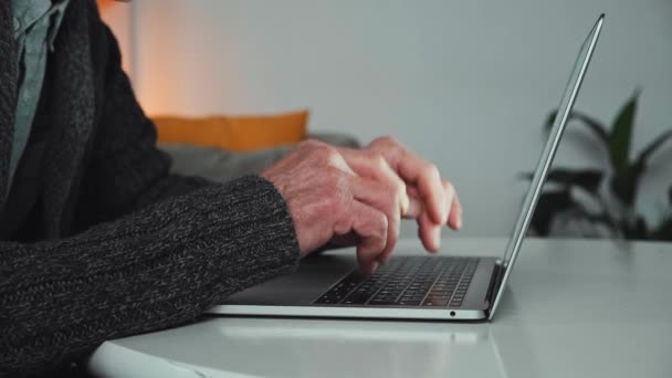 Крупним планом руки старшого чоловіка, що друкує на клавіатурі ноутбука вдома — стокове відео