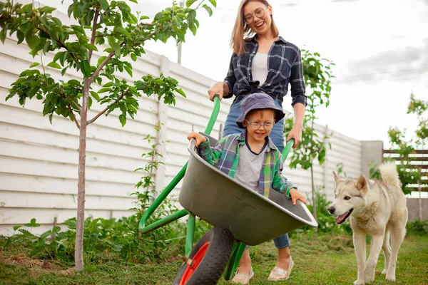 裏庭で楽しい庭のカートに乗る母親と子供 ロイヤリティフリーのストック画像