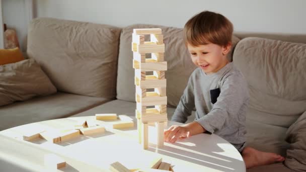 Dziecko rozbił wieżę z drewnianych bloków siedzi na kanapie w domu — Wideo stockowe