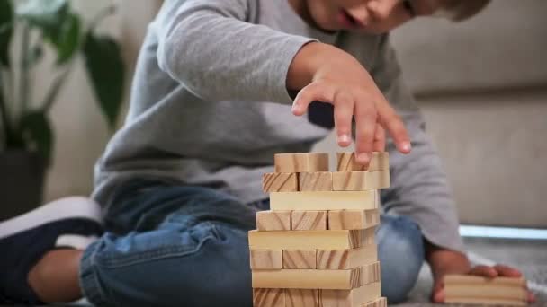 Child builds a wooden tower for playing with wooden blocks sitting on the floor at home — 图库视频影像