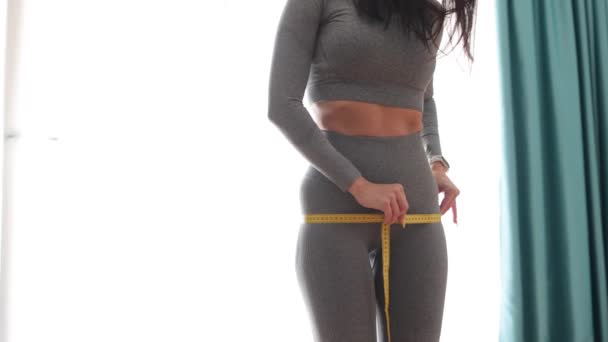 Fitness kvinde måling krop med tape stående foran spejlet derhjemme – Stock-video