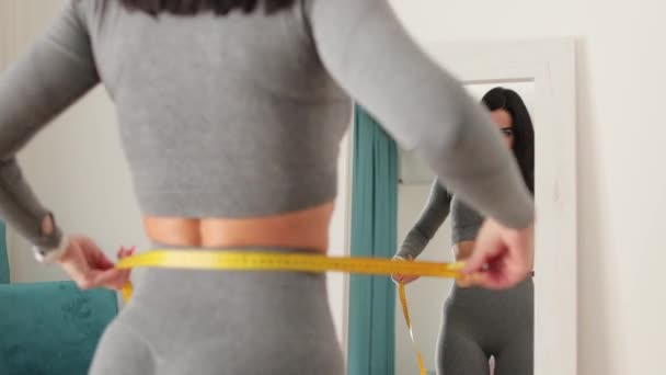 Fitness žena Měřící tělo s páskou stojící před zrcadlem doma — Stock video