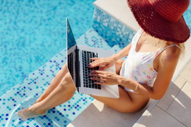 Laptop kullanan ve havuz kenarında çalışan bir kadın.