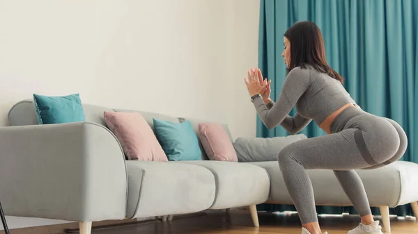 운동 선수인 여자는 집에서 운동을 하고, 쪼그려 앉는다. 가내 부업. — 스톡 사진