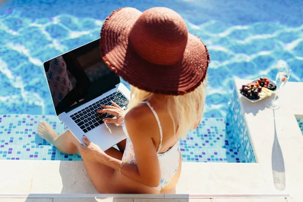 freelancer woman using laptop and work remotely near swimming pool