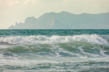 Gün batımının arka planında dağ manzaralı deniz dalgaları