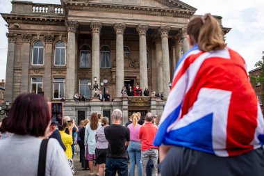 Büyük Britanya bayrağına sarılı genç bir kız, 11 Eylül 202 'de Birkenhead Belediye Sarayı' nda Kral III. Charles Bildirgesi sırasında Wirral Jeff Green 'in Belediye Başkanı olarak konuşmalarını izliyor.