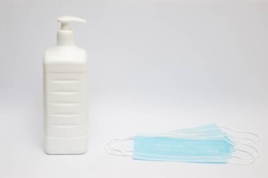 Antiseptik dezenfektan şişesi ve 4 açık mavi cerrahi maske beyaz arka planda duruyor..