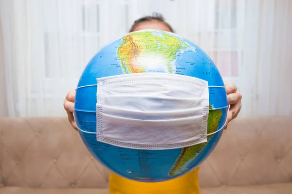The little girl is holding the earth globe in her hands. White surgical mask on earth globe. Pandemic concept. Stay home concept.