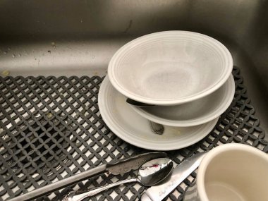 Kirli bulaşıklar ve çatal bıçak seti paslanmaz çelik mutfak lavabosunda gri kauçuk paspas üzerine.