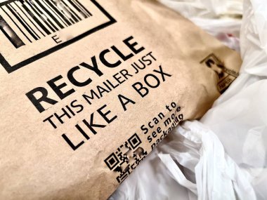 Closeup generic paper package with recycling message amid plastic bags