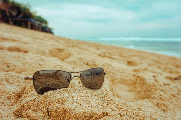 cool sunglasses on the sand with a beautiful ocean sea, green plants and blue sky with clouds on the background at Indrayanti beach in Gunung Kidul, Yogyakarta - Indonesia