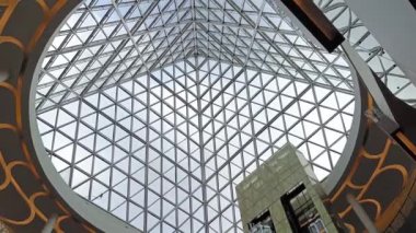 AVM binasının tavanından bakıyorum. Arka planda bir asansör ve üçgen şeklinde modern bir tasarım var.