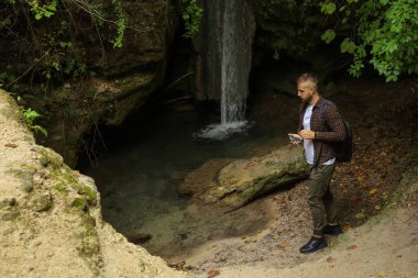 Genç bir adam yol kenarında ve ormanda yürüyor.