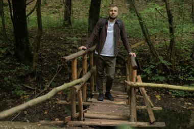 Genç bir adam yol kenarında ve ormanda yürüyor.