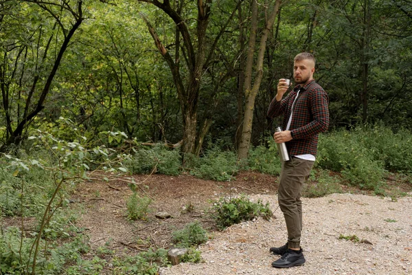 a man walks in the forest, rests and drinks a drink from a thermos