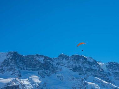 İsviçre 'de karla kaplı bir dağ sırtının önünde bir paraglider.