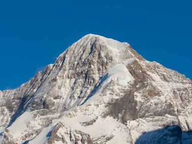 İsviçre 'nin ünlü Moench Tepesi' nin yakın plan profili. Mavi gökyüzünün altında sarp kayalar ve buz duvarları var.