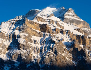 İsviçre 'nin ünlü zirvesi Jungfrau' nun yakın plan profili, mavi gökyüzünün altında sarp kaya ve buz duvarları var.