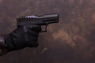 Deri ceketli bir adam elinde deri eldivenli bir silah tutuyor.