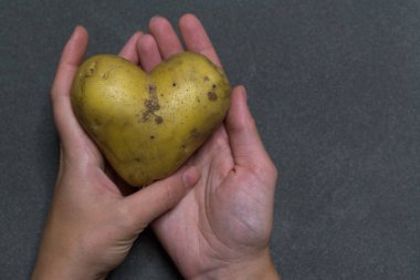 Wonam elleri koyu bir arka planda kalp şeklinde bir patates tutar.