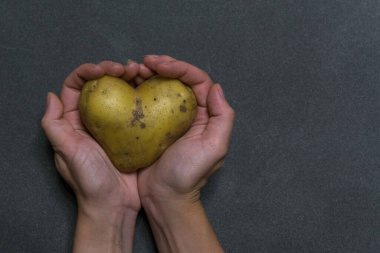 Wonam elleri koyu bir arka planda kalp şeklinde bir patates tutar.