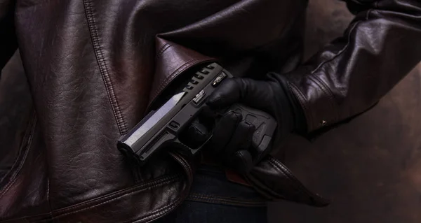 a man in a leather jacket and jeans holds a gun in his hand in a leather glove