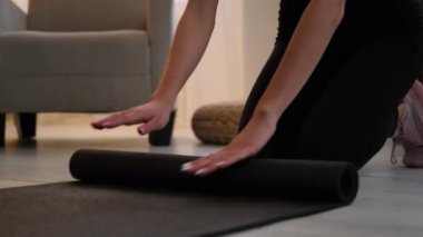 Eğitimden sonra kadın elleri yoga minderi sarar.
