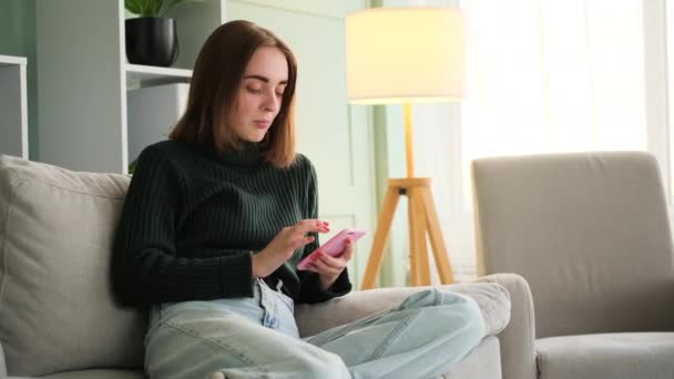 Mladá žena pomocí telefonu sedí na pohovce — Stock video
