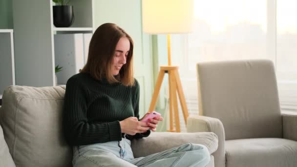 Smějící se žena pomocí telefonu sedí na pohovce — Stock video