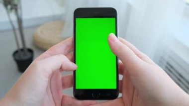 Evde yeşil ekranlı akıllı telefonu tutan kadın.