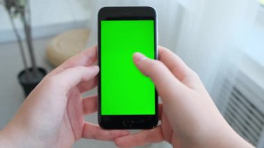 Evde yeşil ekranlı akıllı telefonu tutan kadın.