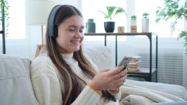 Jonge brunette vrouw zitten sofa, luisteren naar de muziek op de smartphone — Stockvideo