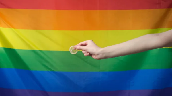Mão segurando um preservativo no fundo da bandeira LGBT Fotos De Bancos De Imagens Sem Royalties