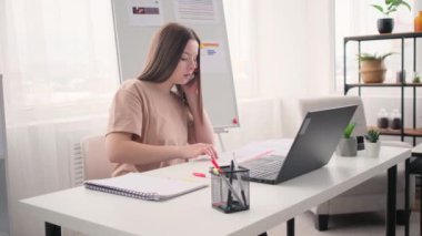 Evrakları kontrol ederken iş kadını evde çalışıyor ve telefonla konuşuyor.