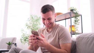 Kanepede oturan adam evde akıllı telefon kullanıyor.