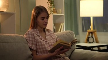 Geceleri kanepede kitap okuyan genç bir kadın.