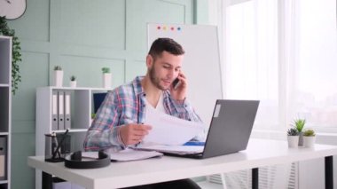 Dizüstü bilgisayarda çalışan ve cep telefonuyla konuşan genç girişimci