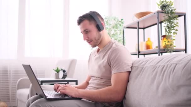 Человек работает из дома сидя на диване и слушать музыку — стоковое видео