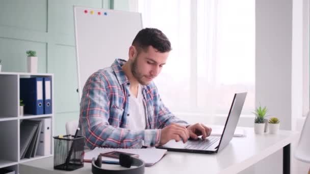 Uomo seduto a lavorare sul computer portatile e parlare sul telefono cellulare — Video Stock