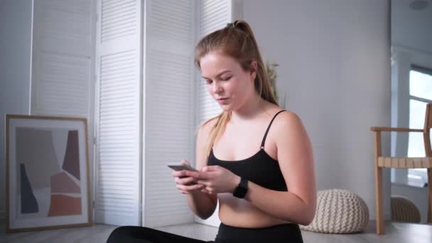 Młoda kobieta SMS-uje na smartfonie po treningu — Wideo stockowe