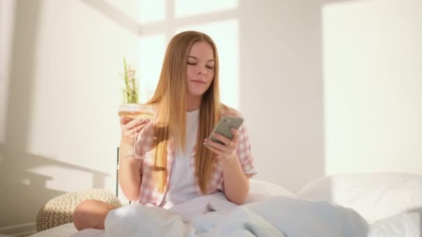 Junge Frau schaut auf ihr Handy und trinkt — Stockvideo