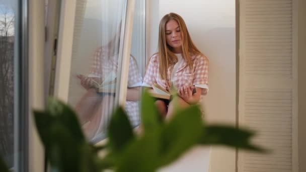 Glückliche Frau liest Buch auf Fensterbank — Stockvideo
