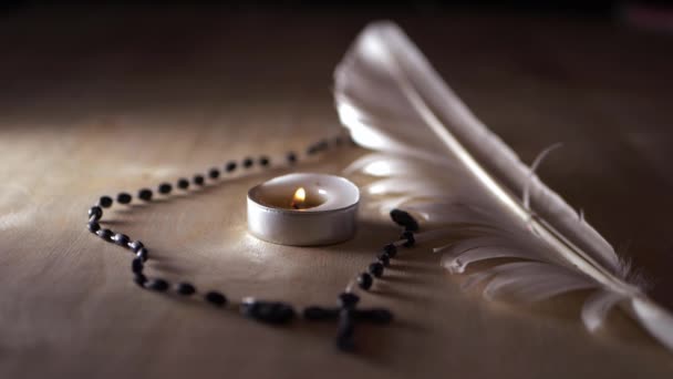 Solitary candle and rosary beads with white feather — Stock Video