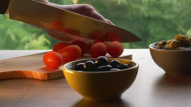 Chopping red cherry tomatoes with olives and pesto — Stock Video