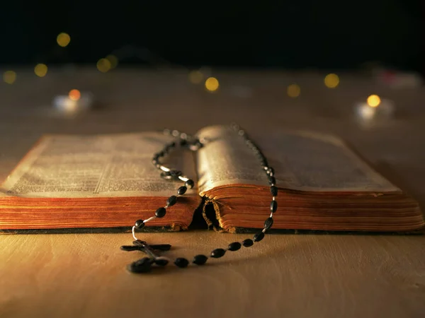 Bible a růženec korálky ve světle svíček bokeh světlo pozadí — Stock fotografie