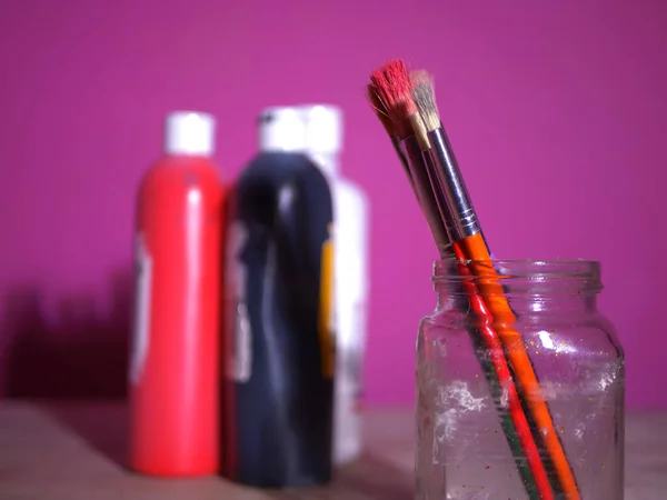 粉红底色玻璃瓶中的画笔和油漆 — 图库照片