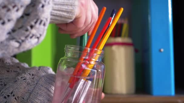 Kunstenaar schoonmaken van penselen in potje water — Stockvideo