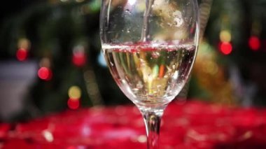 Arka planda Noel ışıkları olan beyaz şarap bardağı dolduruyorum.
